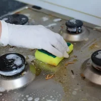domestic-female-hand-wearing-gloves-cleaning-dirty-stove-after-cooking-using-sponge-washing-woman-housewife-enjoying-daily-household-closeup-top-view_132075-13125
